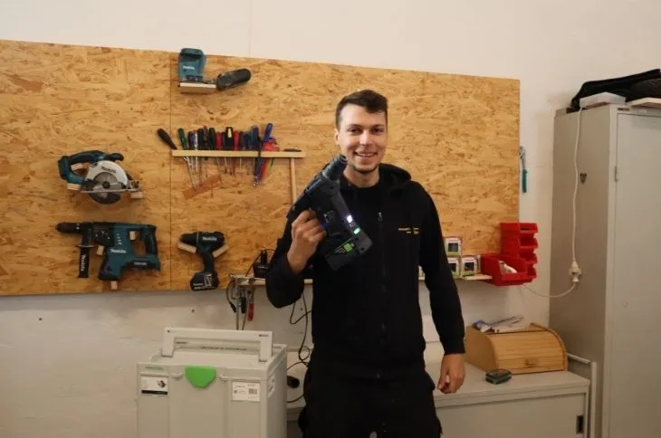 gluecklicher umzugshelfer haelt bohrmaschine in werkstatt